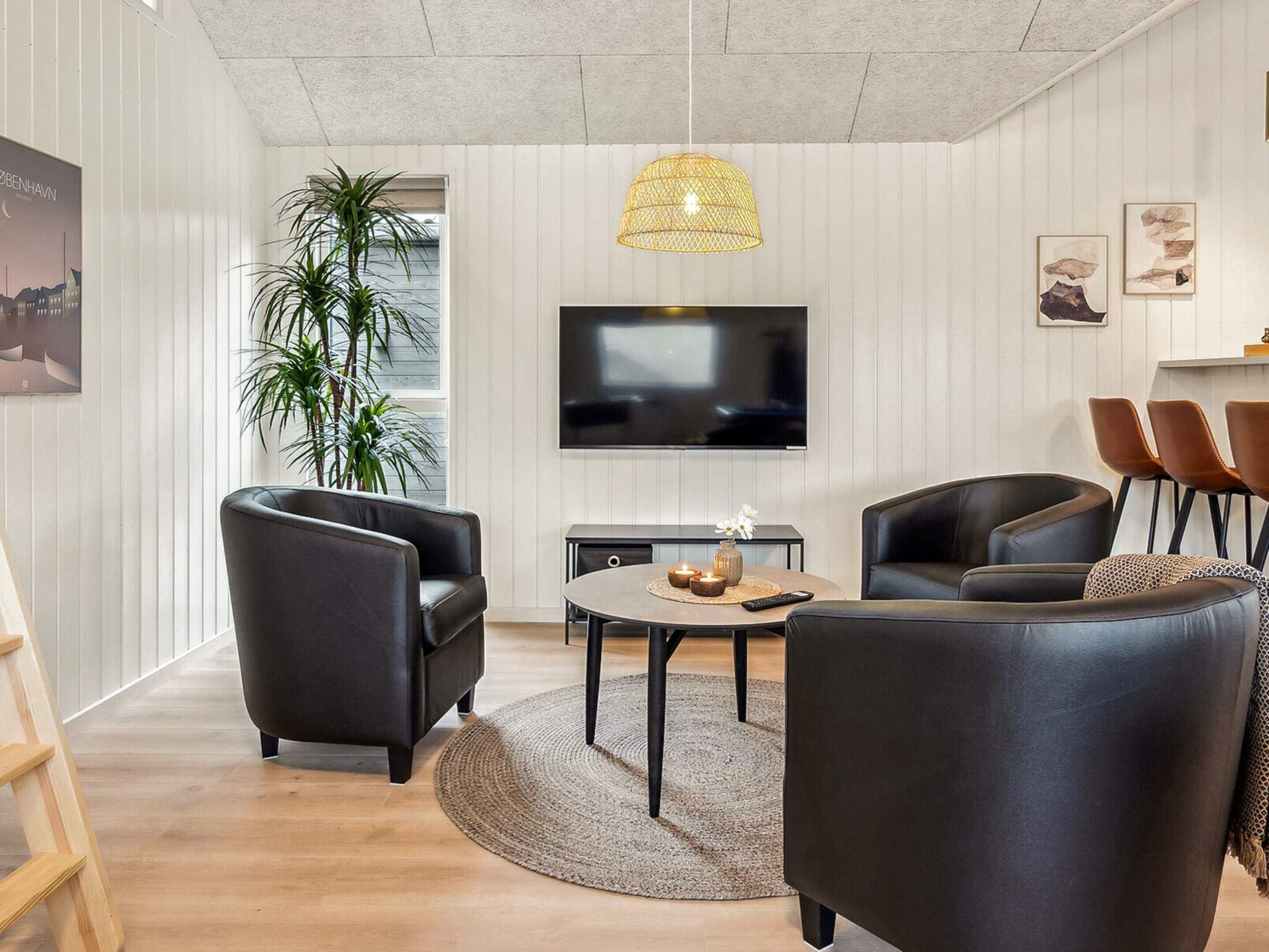 Ein modernes Wohnzimmer mit einem Flachbildfernseher, Ledersofas, einem runden Couchtisch und einer großen Küstpflanze.