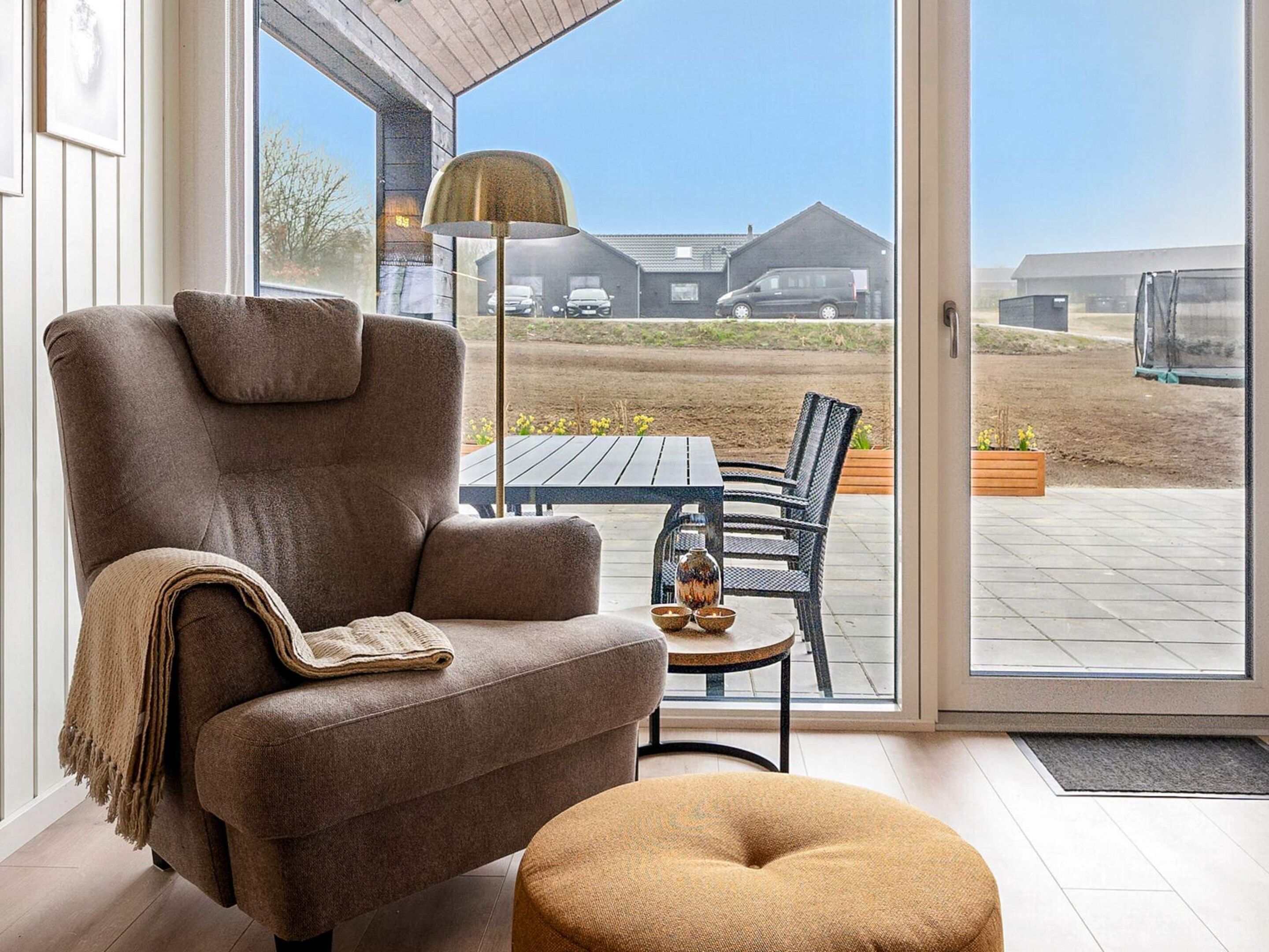 A modern living room with a brown armchair, a small ottoman, and a dining table with chairs.