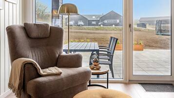 A modern living room with a brown armchair, a small ottoman, and a dining table with chairs.