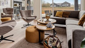 A modern living room with a sofa, armchairs, and ottoman, a coffee table, and a large window with a view of the outside. - 5 Star Holiday Home in Sydals (Sydals)