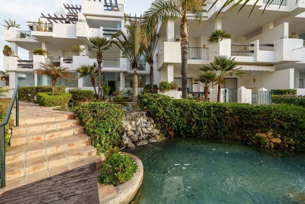 A modern building with multiple balconies, a small water feature, and a paved pathway leading to the entrance. - Cozy Apartment in La Cala de Mijas (Mijas)