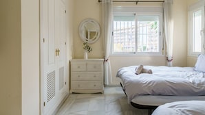Een slaapkamer met een bed, een dressoir, een spiegel en een raam met gordijnen.
