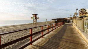 Een houten looppad dat naar een strand leidt, met een badwachterstoeltje en een gebouw met de tekst 