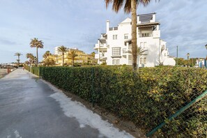 A coastal residential area with a paved walkway, a tall white building with balconies, and palm trees. - Cozy Apartment in La Cala de Mijas (Mijas)