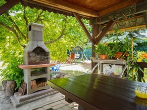 An outdoor patio with a stone-built pizza oven, wooden tables, and potted plants. - Noisette by Interhome (Balatonkeresztur)