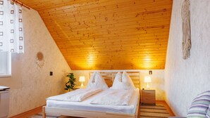 A cozy bedroom with a wooden ceiling, a bed with white linens, two bedside lamps, and a macrame wall hanging. - Noisette by Interhome (Balatonkeresztur)
