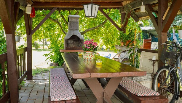 An outdoor wooden pergola with a stone pizza oven, picnic table, benches, and potted plants. - Noisette by Interhome (Balatonkeresztur)