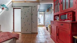 A room with a bed, a red cabinet with a microwave, a door with a rain pattern, and a window with blinds. - Faro's Casa Evita - Estepona Old Town (Estepona)