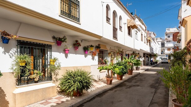 A narrow street lined with white buildings, each adorned with potted plants and featuring balconies with metal railings. - Faro's Casa Evita - Estepona Old Town (Estepona)