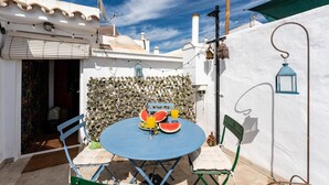 A patio with a round table, two chairs, a watermelon, and a glass of orange juice. - Faro's Casa Evita - Estepona Old Town (Estepona)