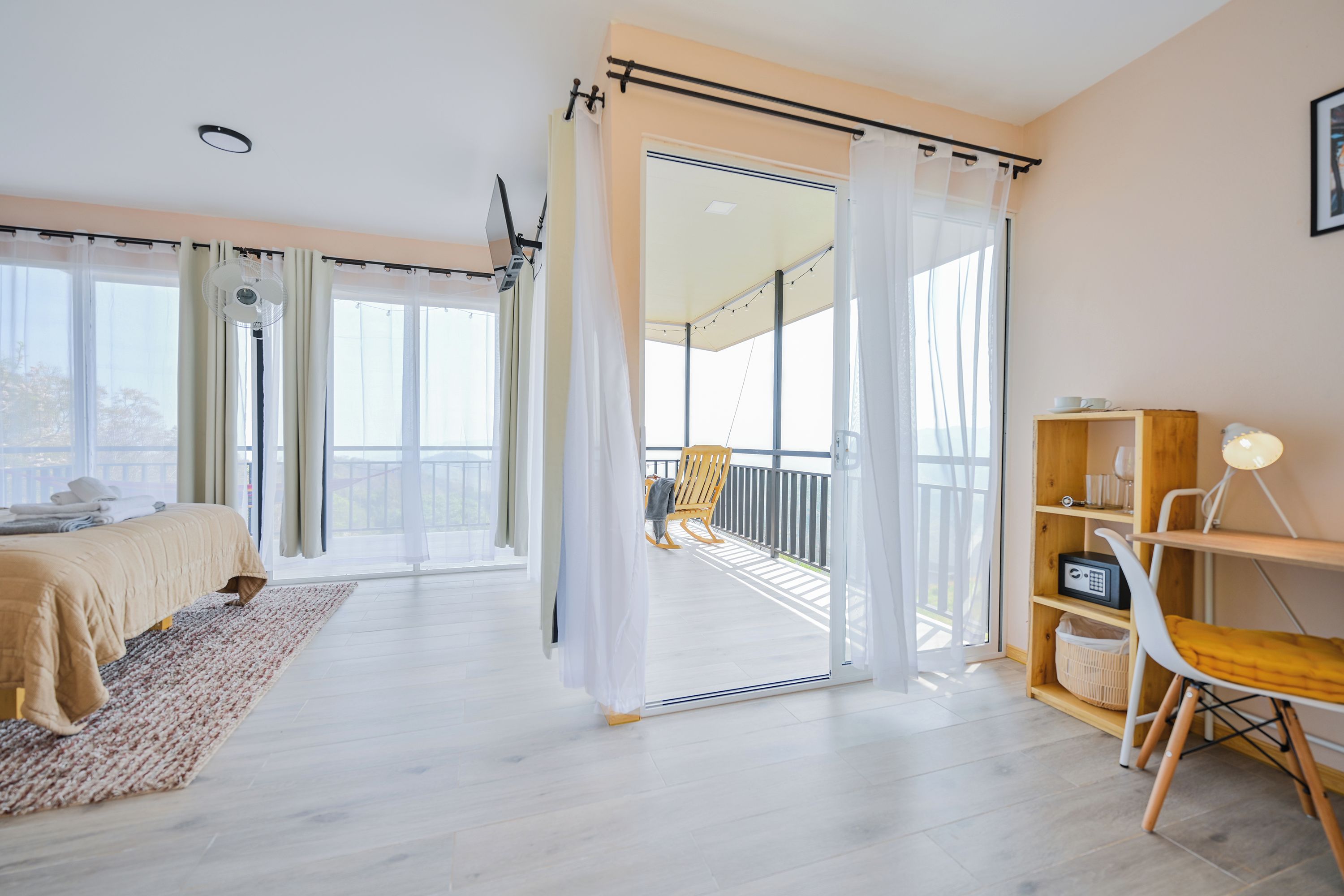 A modern bedroom with a bed, a wooden chair, a small table, and a balcony with a view.
