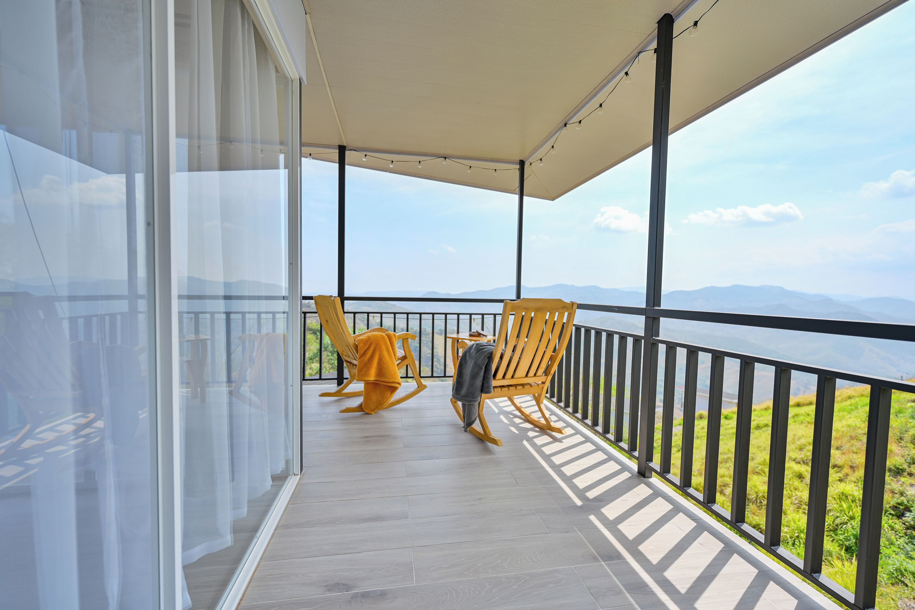 A balcony with two rocking chairs, a glass door, and a view of mountains.