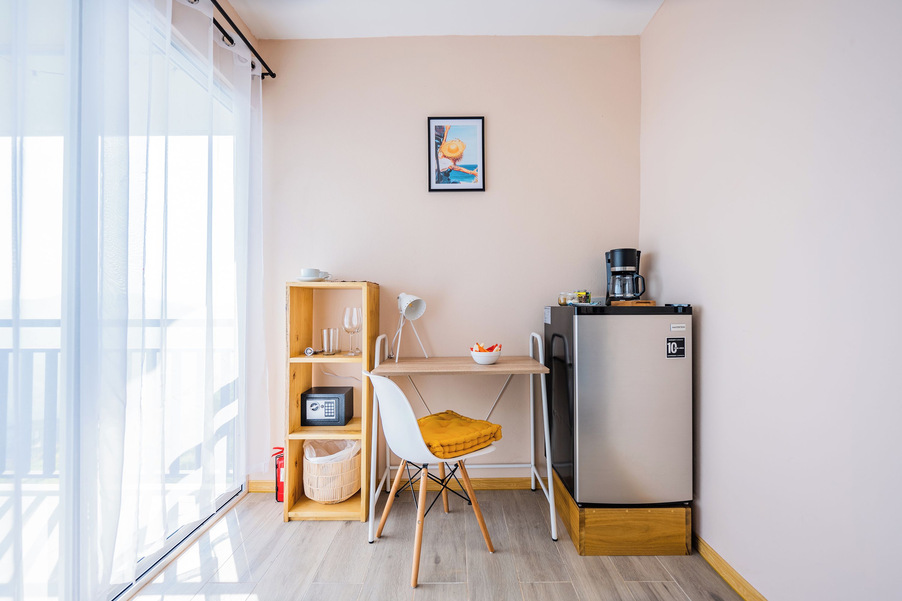 A compact kitchenette with a refrigerator, a coffee maker, and a small table with a chair.