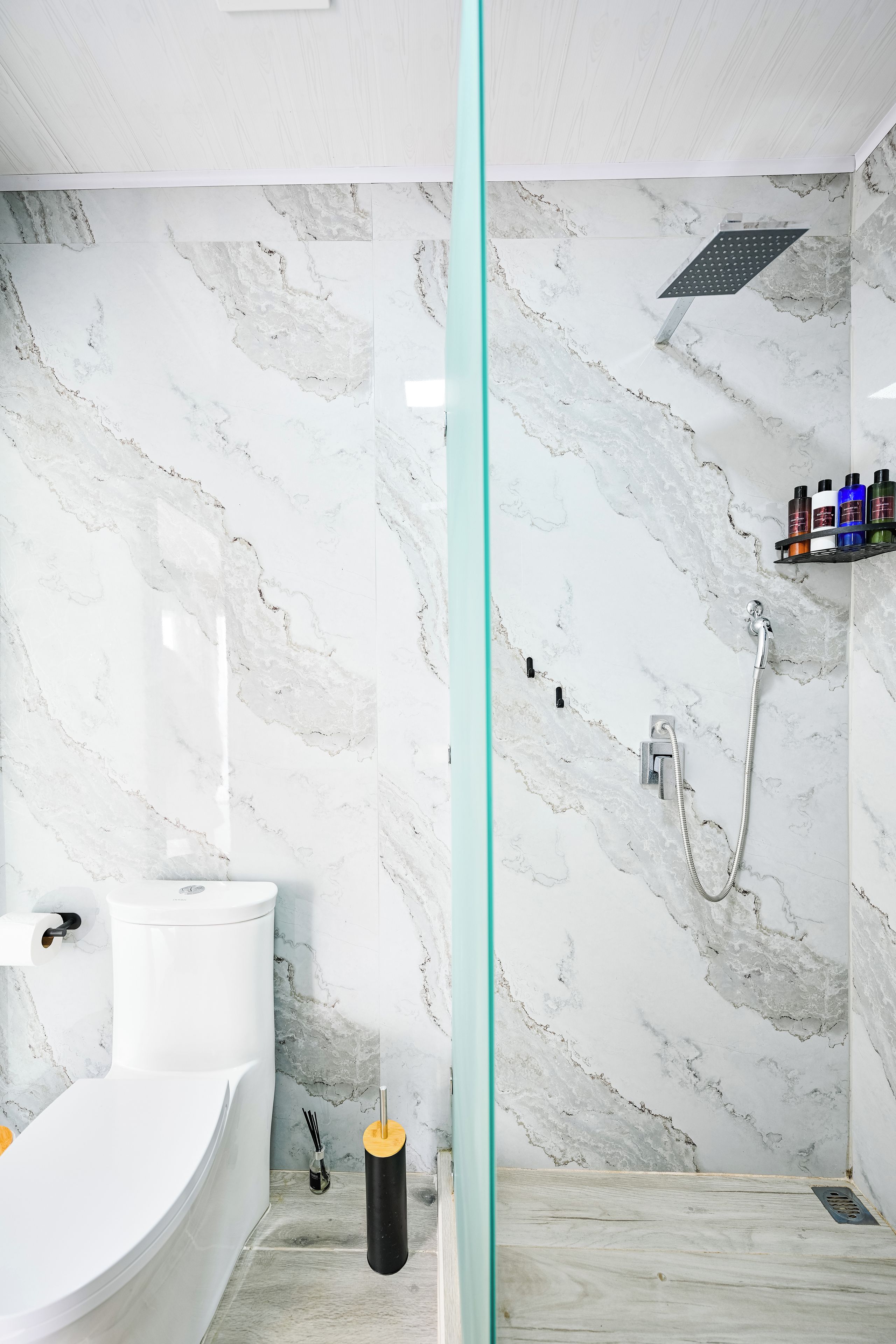 A bathroom with a bathtub, toilet, shower, and marble walls.