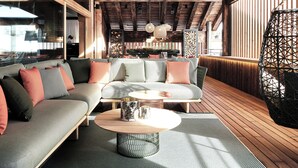A cozy, well-lit living area with a wooden ceiling, a large sectional sofa, and a round coffee table. - Lech Lodge - LEGENDARY (Lech am Arlberg)