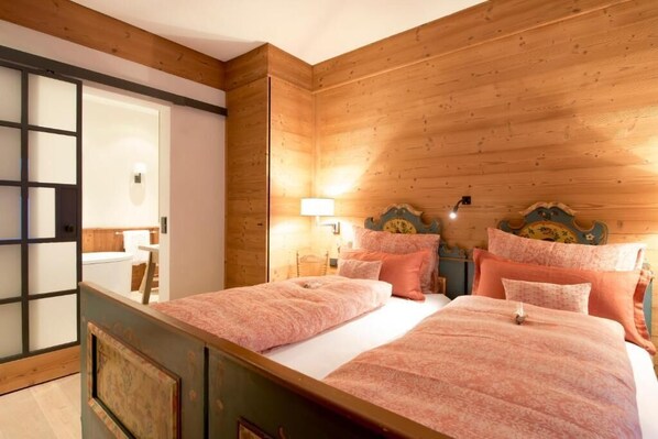 A bedroom with two beds, wooden paneling on the walls, and a sliding door leading to a bathroom. - Lech Lodge - LEGENDARY (Lech am Arlberg)