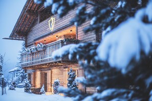 Eine Holzchalet mit Balkon, schneebedeckten Bäumen und einem beleuchteten Schild über dem Eingang.