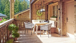 A wooden deck with a table and chairs, surrounded by potted plants and a scenic mountain view. - Lech Lodge - LEGENDARY (Lech am Arlberg)