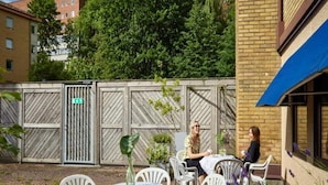An outdoor seating area with white plastic chairs and tables, a wooden fence with a gate, and a building with a blue awning. - 6 Person Holiday Park Home in Goteborg (Gothenburg)