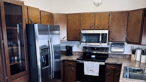 A kitchen with wooden cabinets, stainless steel appliances, a granite countertop, and a clock on the wall. - Authentic Spearfish Home 1 Block from Black Hills State-- Sleeps 8 (Spearfish)