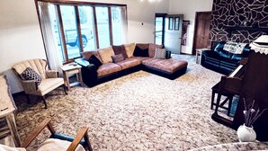 A spacious living room with a large sectional sofa, a piano, and a stone accent wall. - Authentic Spearfish Home 1 Block from Black Hills State-- Sleeps 8 (Spearfish)