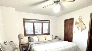 A bedroom with a bed, a nightstand, a chair, a window, a door, and a ceiling fan. - Authentic Spearfish Home 1 Block from Black Hills State-- Sleeps 8 (Spearfish)