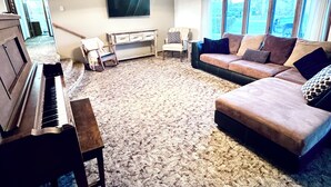 A living room with a piano, sofa, and large windows. - Authentic Spearfish Home 1 Block from Black Hills State-- Sleeps 8 (Spearfish)