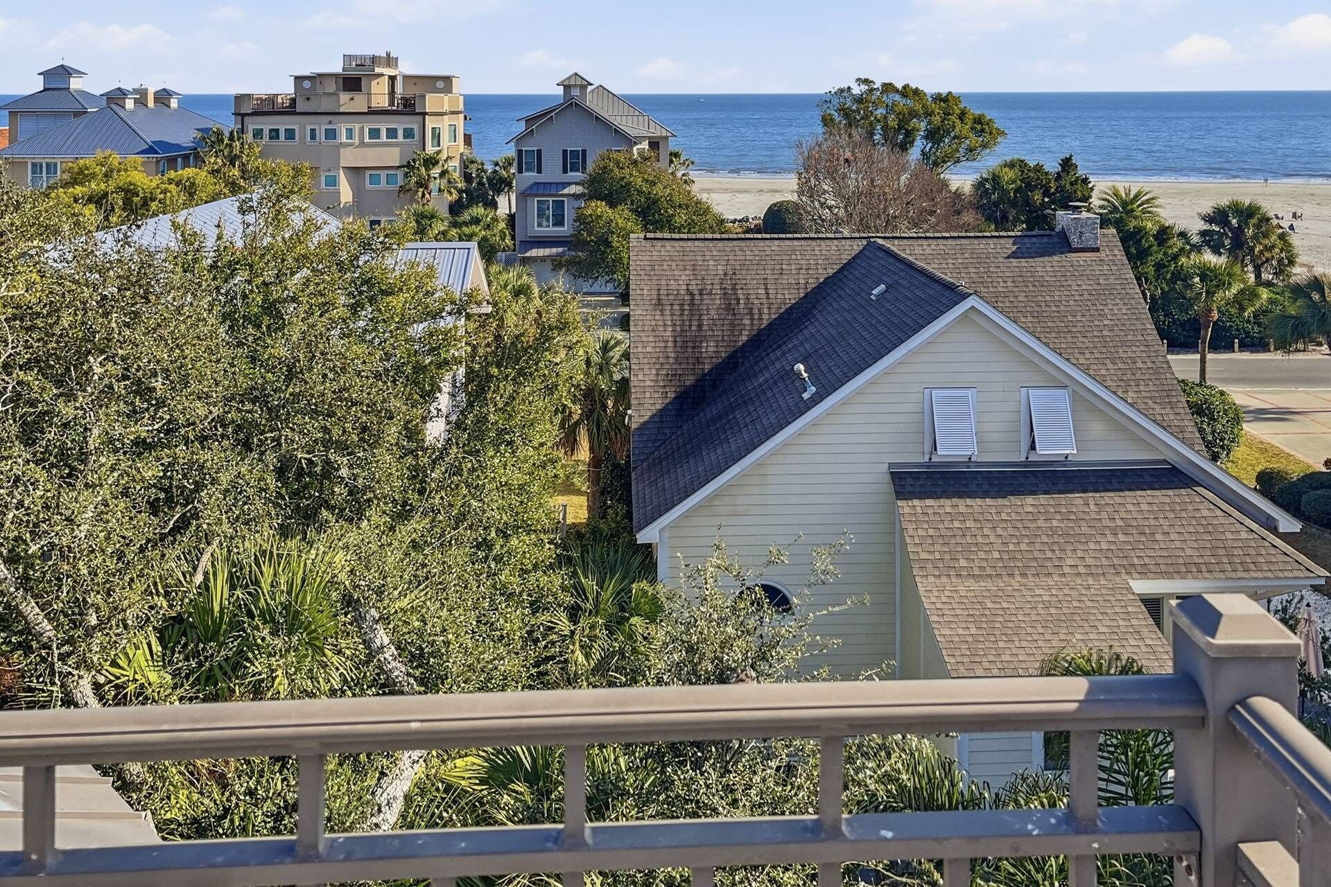 A residential area with a house overlooking a beach, surrounded by other buildings and dense foliage.