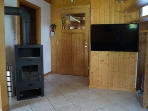 A room with a black fireplace, wooden walls, a tiled floor, a wooden door, and a mounted TV. - # 31 mit 2 Schlafzimmern für 6 Personen by Interhome (Sankt Georgen am Kreischberg)