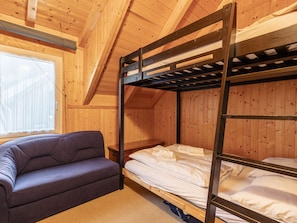 Ein Schlafraum mit Etagenbetten, einer Schlafcouch, Holzwänden und einem Fenster.