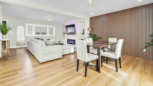 Un salon moderne avec un canapé blanc, une table à manger et des chaises, un plancher en bois et un téléviseur.