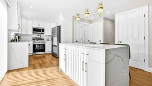 Une cuisine moderne avec des meubles blancs, un îlot central, des appareils en acier inoxydable et des luminaires suspendus.