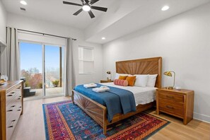 A bedroom with a large bed, a nightstand, a dresser, a ceiling fan, and a view through a sliding glass door.
