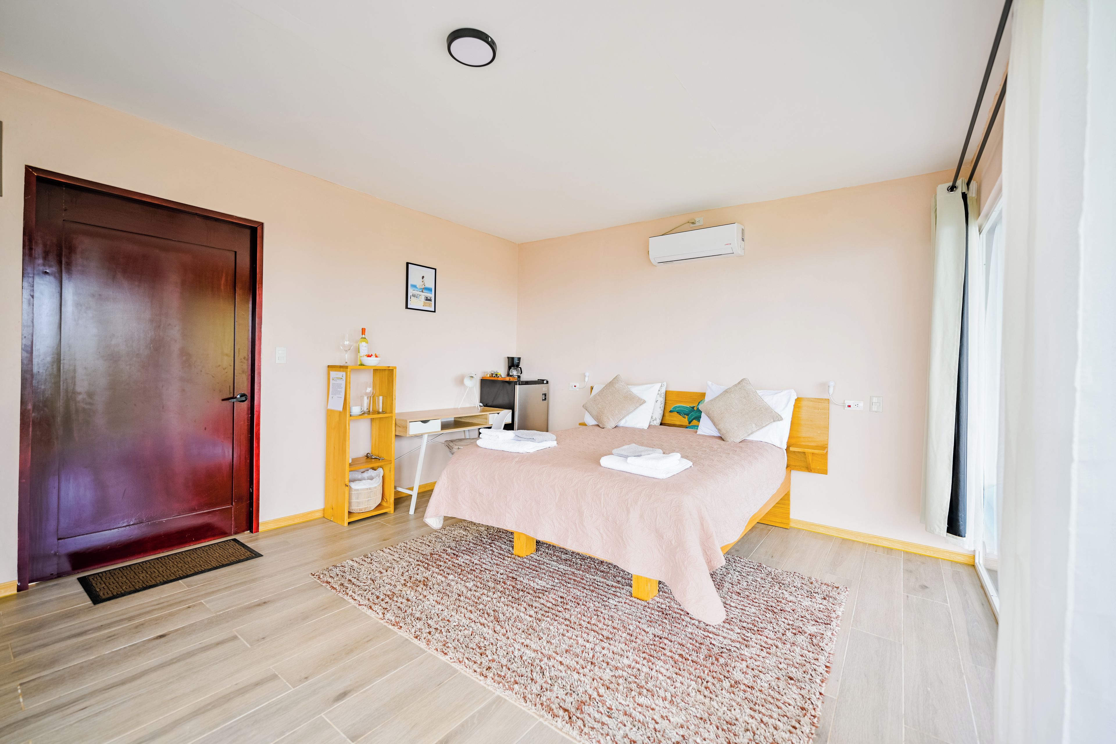Une chambre à coucher avec un lit, un bureau, une armoire, une porte et une fenêtre.