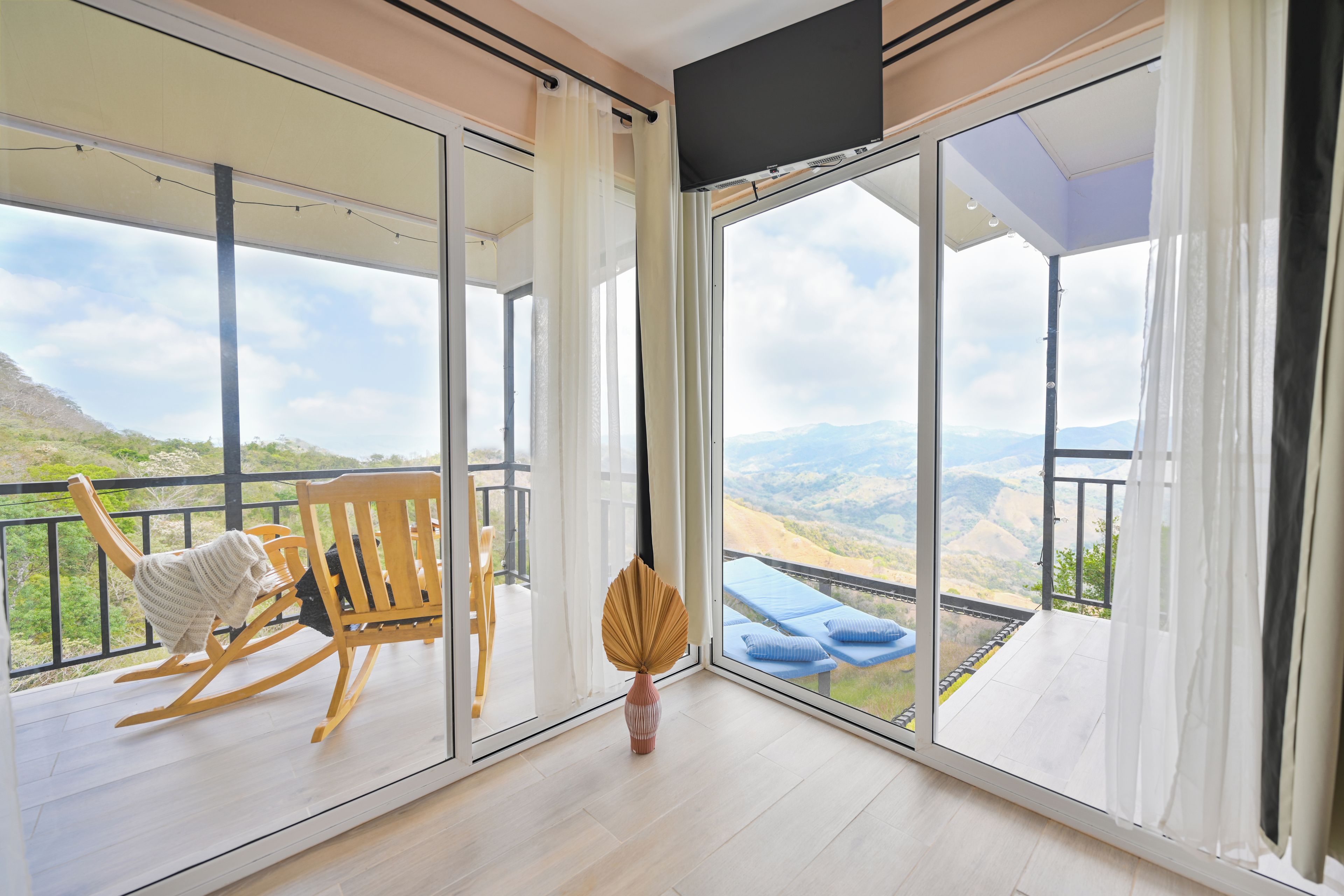 Un balcon avec une chaise en bois et un vase, donnant sur un paysage montagneux.