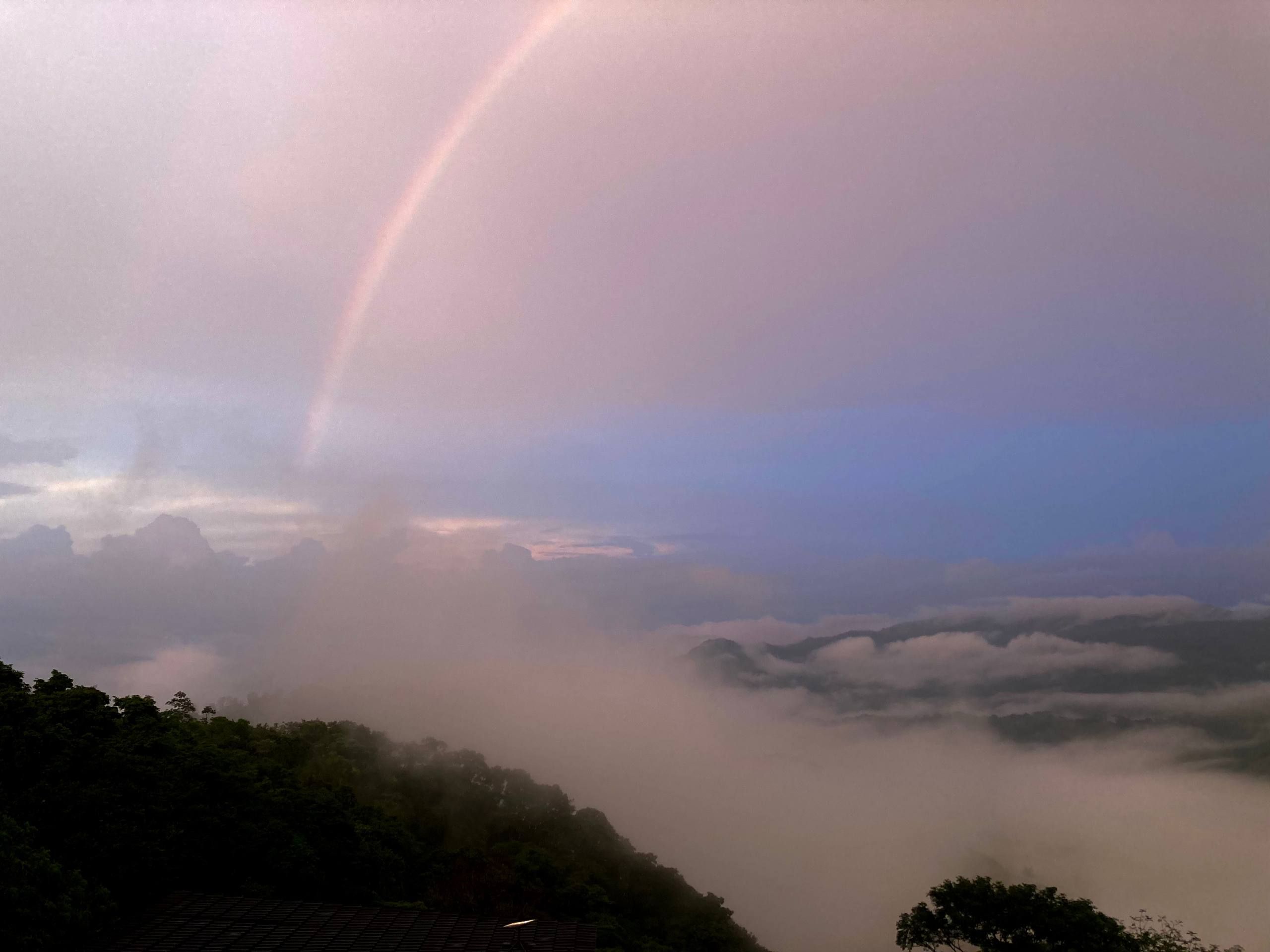 A landscape with a rainbow, clouds, and a forested area.