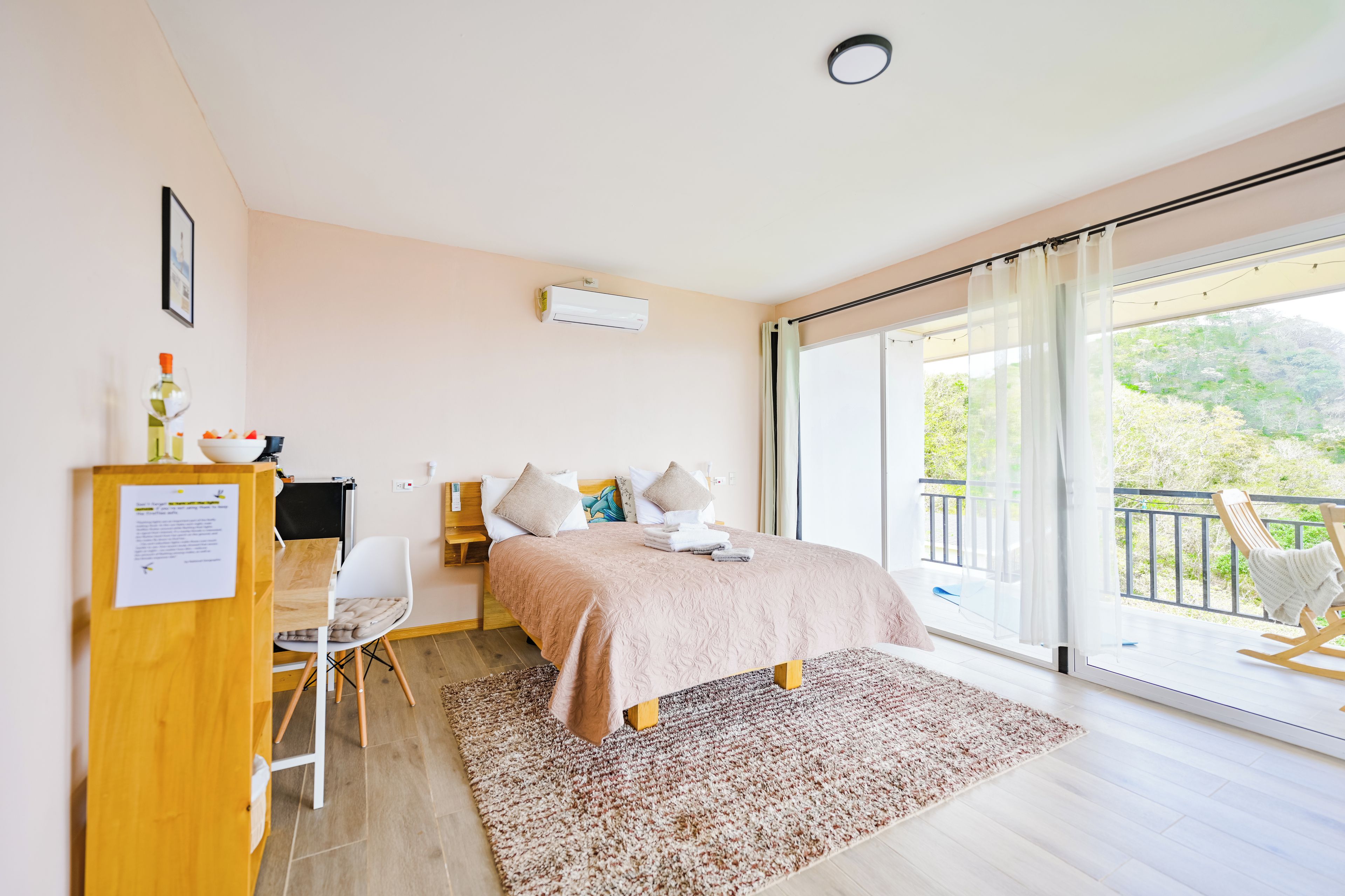 Une chambre à coucher avec un lit, un bureau, une chaise, une fenêtre et un balcon.