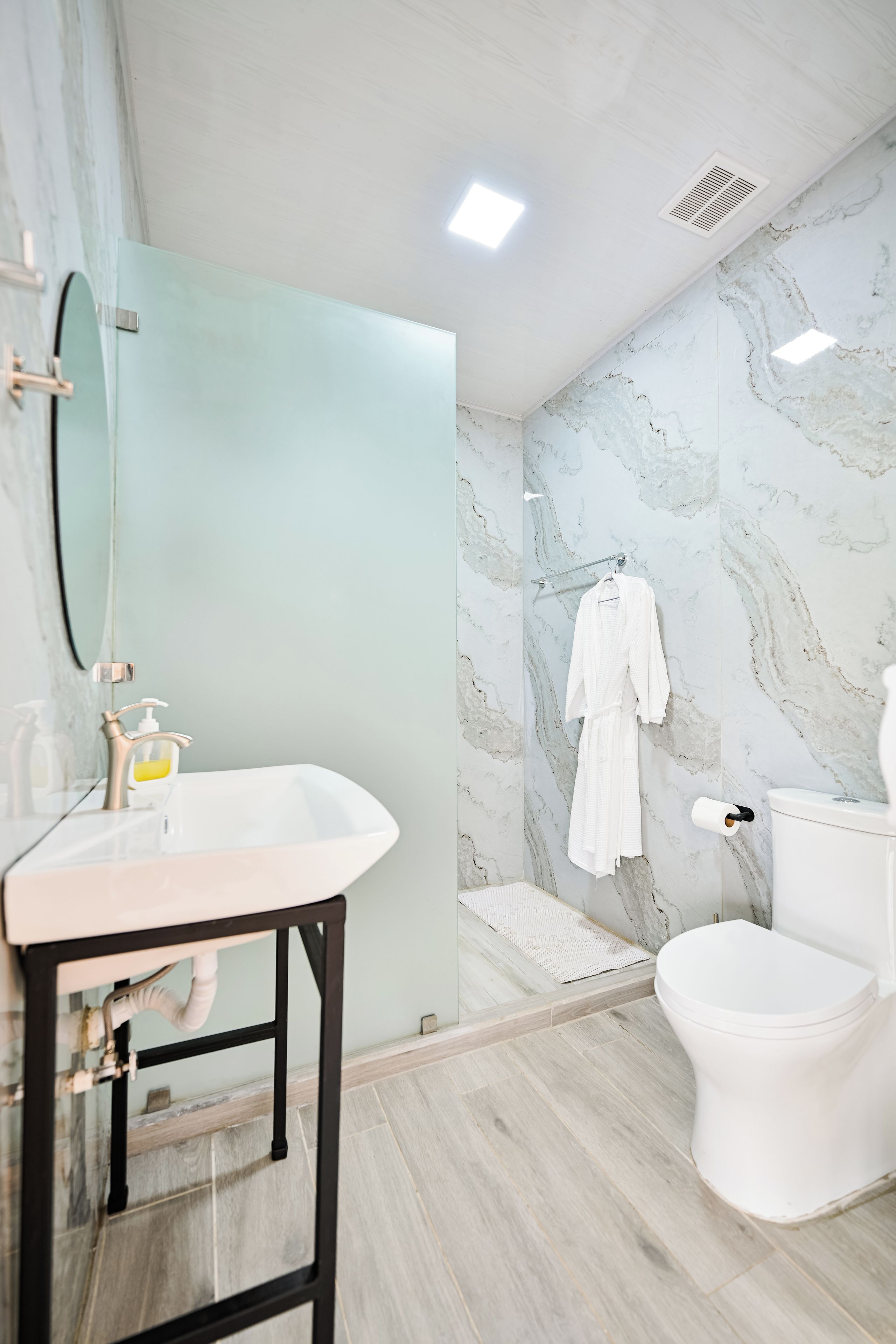 Ein modernes Badezimmer mit Marmorwand, Waschbecken in Weiß, Toilette und Handtuch.