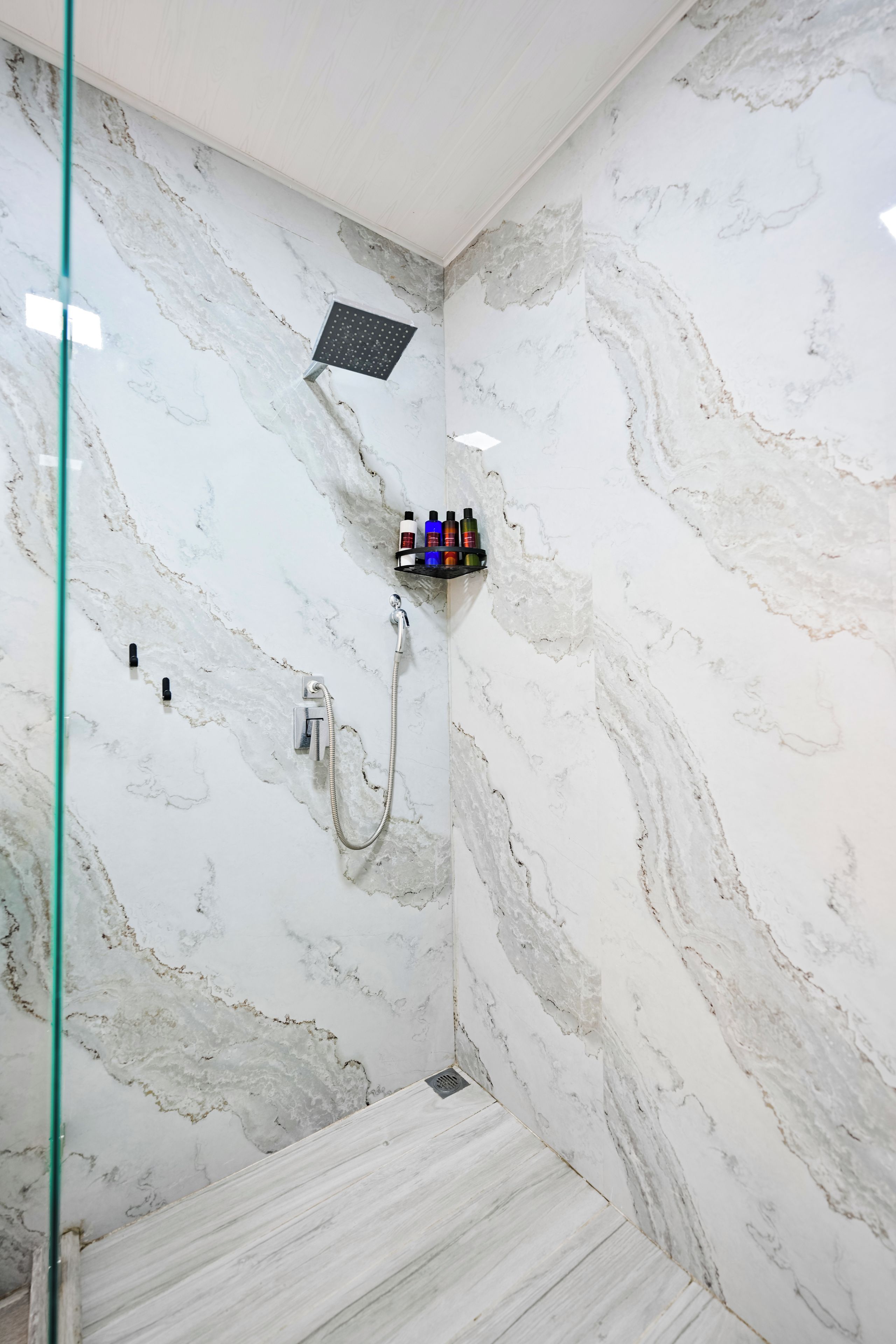 Un baño con ducha, mampara de vidrio y un estante con artículos de aseo.