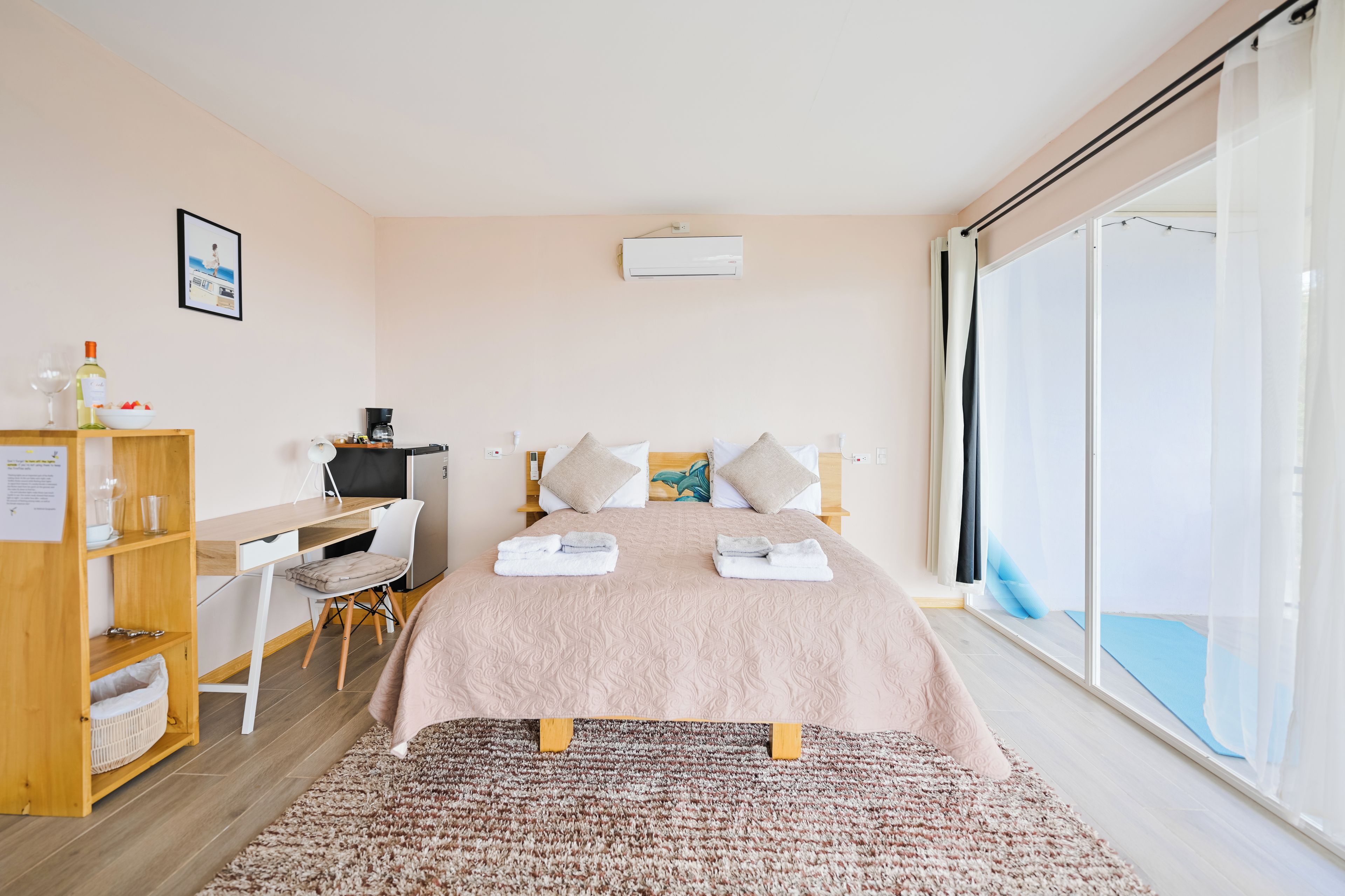 Une chambre d’hôtel avec un lit, un bureau, une chaise, une petite table avec une bouteille et des verres, et une fenêtre donnant sur un paysage agréable.