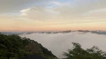 Un paysage montagneux offrant une vue sur une zone boisée et sur un bâtiment doté d’un toit sombre.