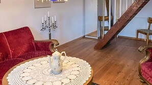 A cozy living room with a red velvet sofa, a wooden coffee table with a white doily, a white pitcher, and a candelabra with candles. - 4 Star Holiday Home in Munka-ljungby (Munka-Ljungby)