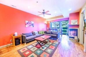 A living room with a sofa, coffee table, and a colorful rug. There is a fireplace and a ceiling fan.