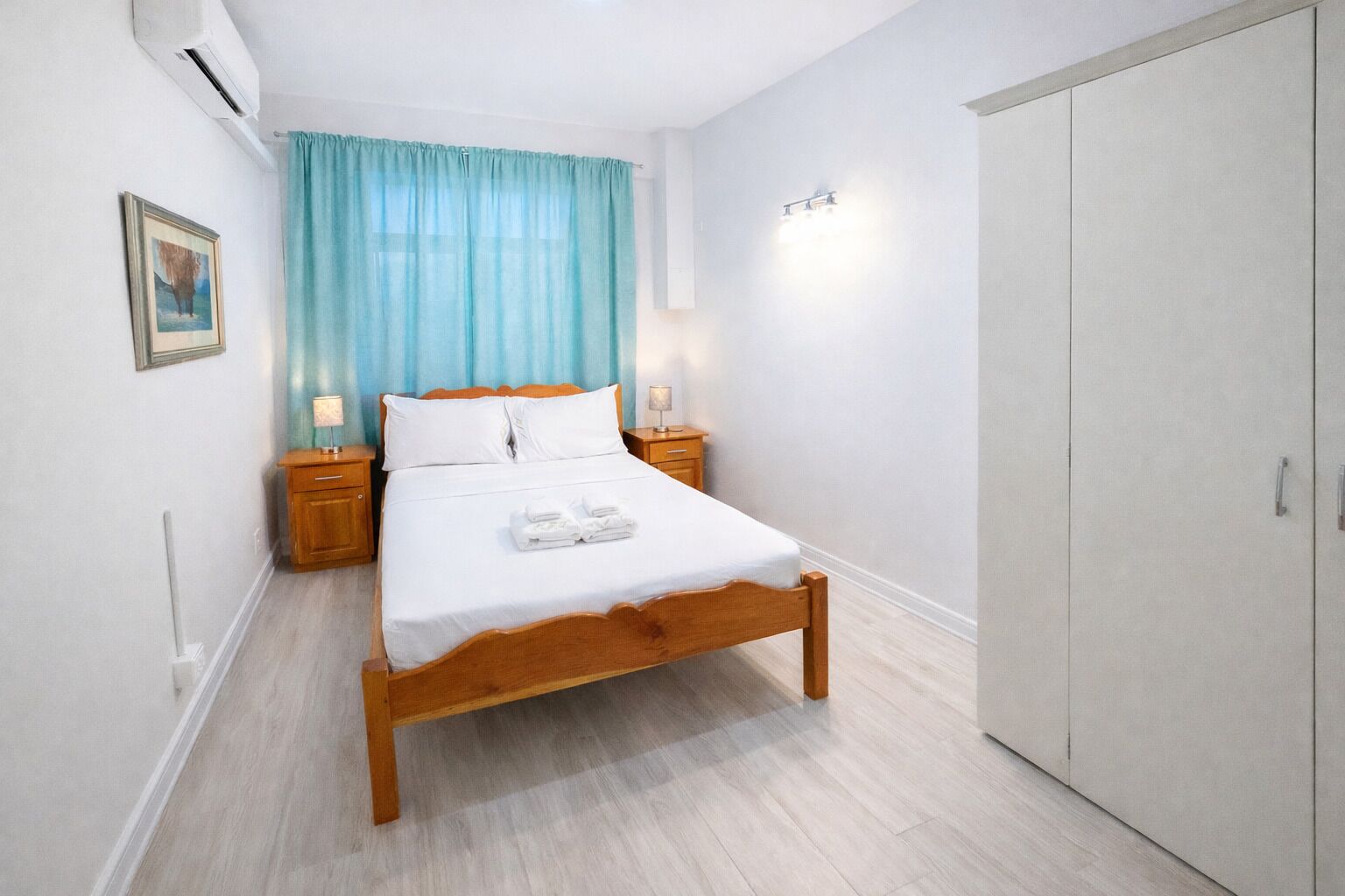 A bedroom with a wooden bed, two bedside tables, a nightstand, a wardrobe, and a window with blue curtains.