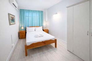 A bedroom with a wooden bed, two bedside tables, a nightstand, a wardrobe, and a window with blue curtains.