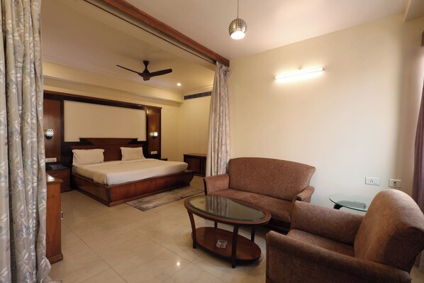 A hotel room with a bed, a sofa, a glass-top coffee table, a ceiling fan, and a wall-mounted light fixture. - Vibe Vacation Hotel, Visakhapatnam – Stay in the Heart of the City (Visakhapatnam)