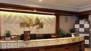 A reception desk with a wooden finish, a wall-mounted decorative panel, and a sign indicating 'Reception.' - Vibe Vacation Hotel, Visakhapatnam – Stay in the Heart of the City (Visakhapatnam)