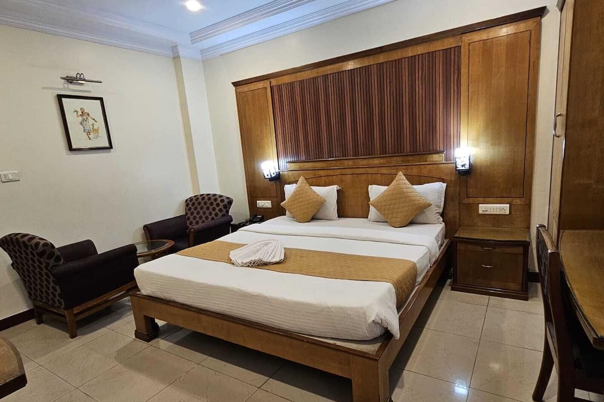 Habitación de hotel con una cama grande, dos mesitas de noche, cabecero de madera, una silla y una pequeña mesa.