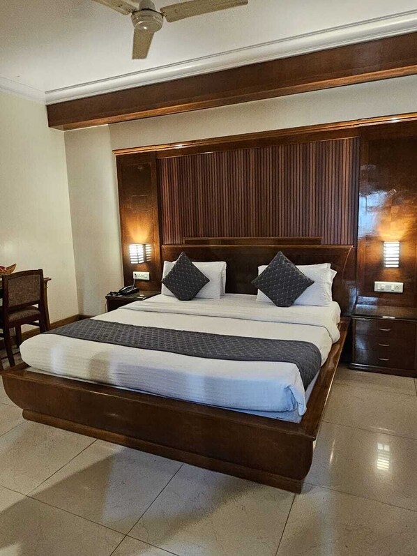 A large bed with a wooden headboard, two bedside tables, and a ceiling fan. - Vibe Vacation Hotel, Visakhapatnam – Stay in the Heart of the City (Visakhapatnam)