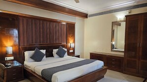A bedroom with a wooden bed, nightstands, a dresser, and a mirror. - Vibe Vacation Hotel, Visakhapatnam – Stay in the Heart of the City (Visakhapatnam)